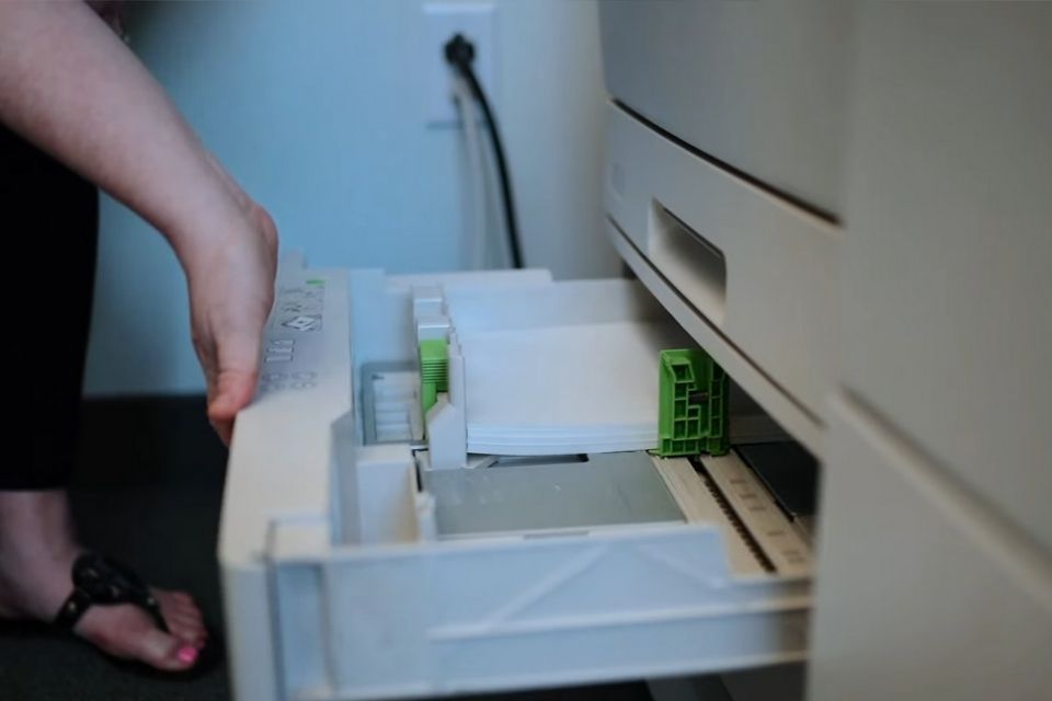 Ruka izvlači fioku štampača i namešta beli papir za štampanje